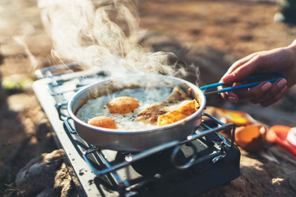 eggs cooking in a pan on a small camp stove-cooking gear is a camping essential