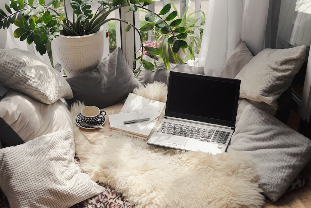 cozy hygge nook used as a workspace with a potted plant, blankets and pillows
