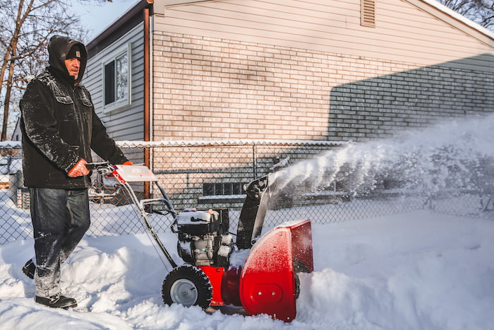 A man clears a driveway using a snowblower