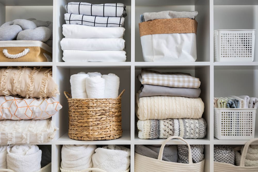 organized linen closet with baskets, bins and folded linens