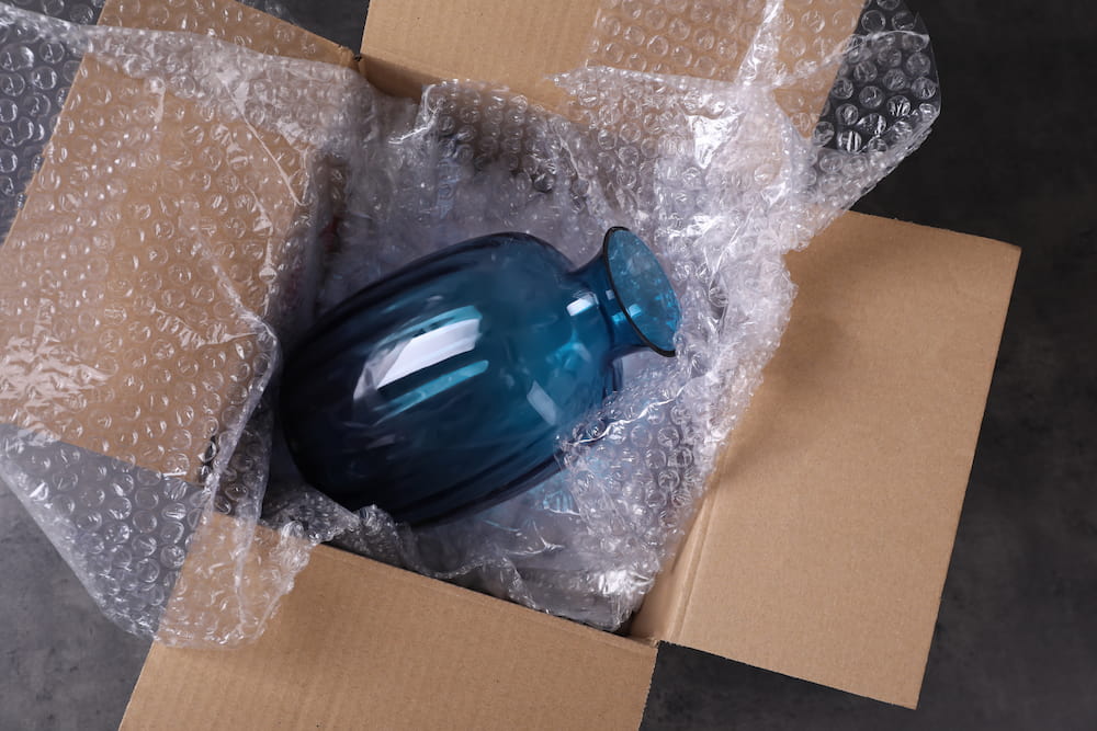 blue vase wrapped in bubble wrap in a cardboard box packed for moving