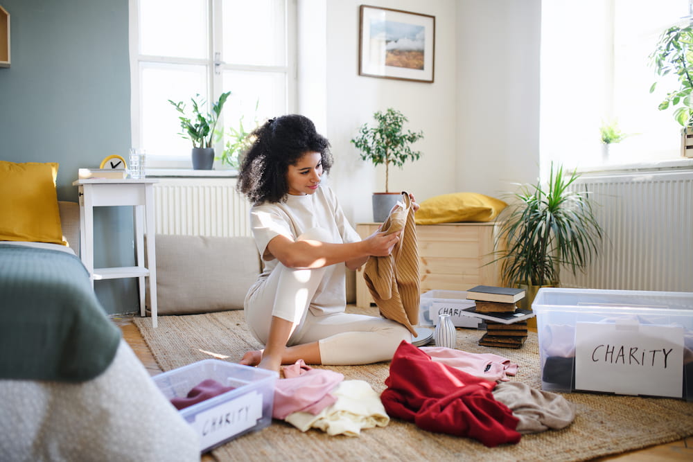 woman sitting on bedroom floor decluttering clothes