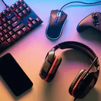 A computer keyboard, mouse, gaming controller, over the ear headphones, and a phone.