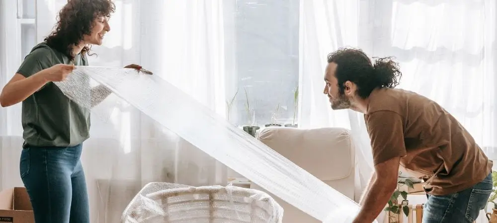 A man and woman wrapping furniture in bubble wrap.
