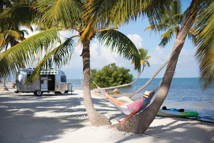 a man rests in a hammock on a beach near his camper