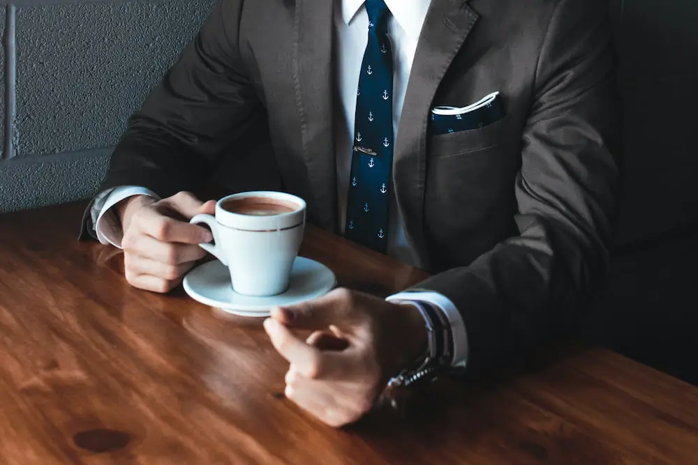 A man in a suit drinks a cup of coffee.