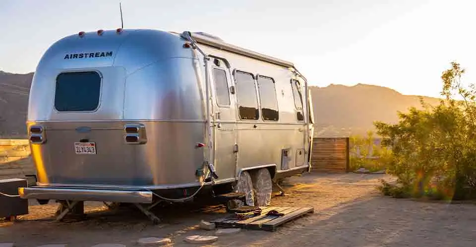 An Airstream camper is parked in a campground with a pretty sunset out of camper storage