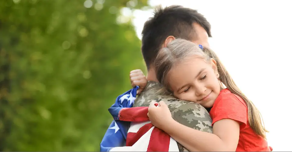 Celebrating Memorial Day, a daughter hugs her military father with an American Flag.
