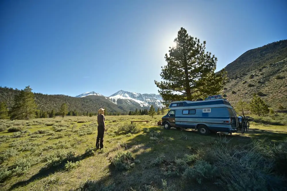 blue and black RV sitting in a meadow with snow-capped mountains rising in the background