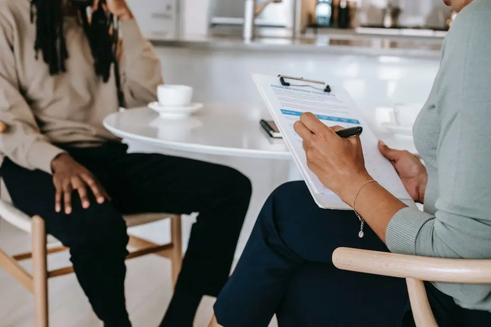 vantage point of a interview. two women sitting at a round table with clipboard and cup of coffee.