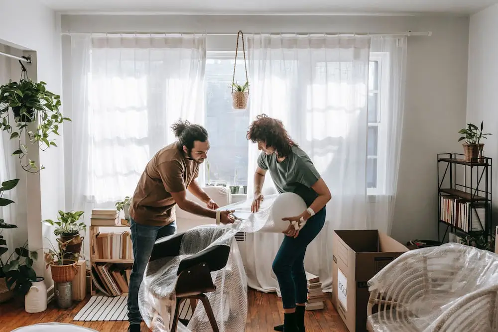 a couple wraps a chair in bubble wrap in preparation for storage