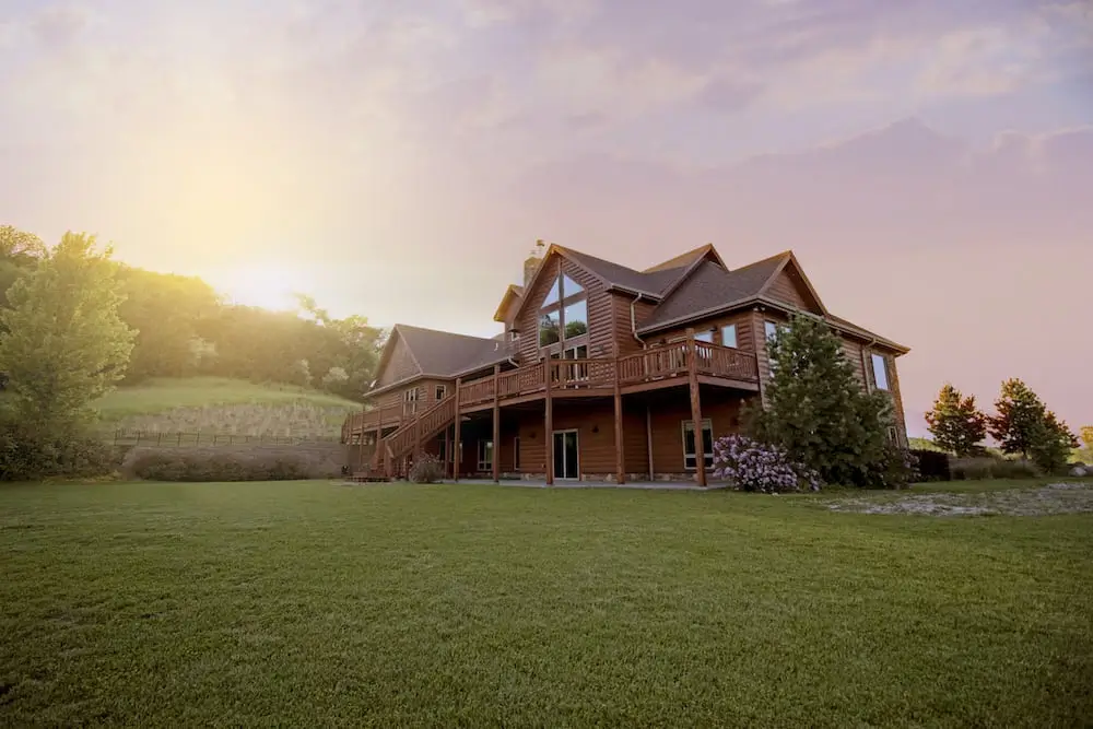 low vantage point of a log home sitting on a green hillside as the sun sets behind it