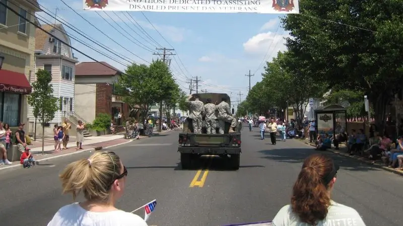 A parade with people in army uniforms in the back of a truck.
